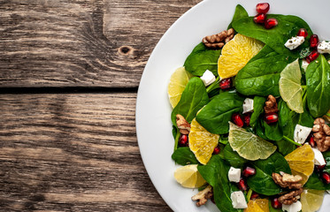 Spinach salad, orange, lemon, pomegranate, feto cheese, walnut on a white plate on a wooden table