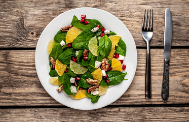 Spinach salad, orange, lemon, pomegranate, feto cheese, walnut on a white plate on a wooden table