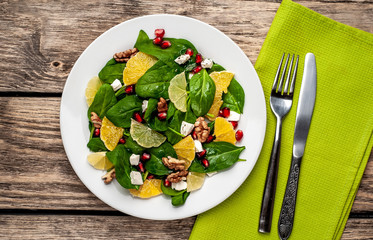 Spinach salad, orange, lemon, pomegranate, feto cheese, walnut on a white plate on a wooden table