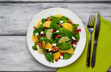 Spinach salad, orange, lemon, pomegranate, feto cheese, walnut on a white plate on a wooden table