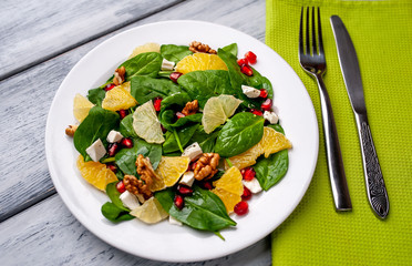 Spinach salad, orange, lemon, pomegranate, feto cheese, walnut on a white plate on a wooden table