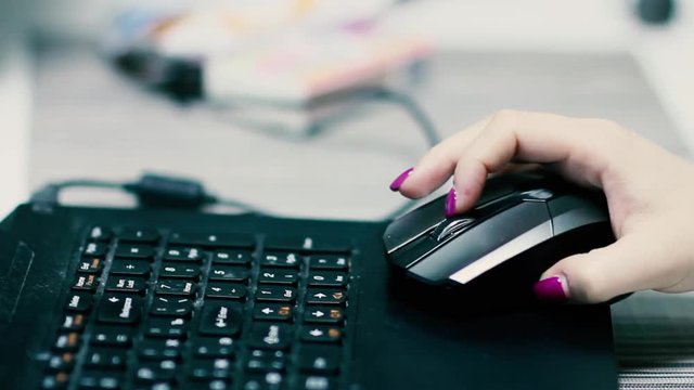 female hand uses a computer mouse, scrolling while working behind a laptop.