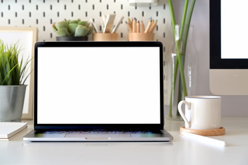 Office desk scenery with mockup blank screen laptop computer. Workspace minimal