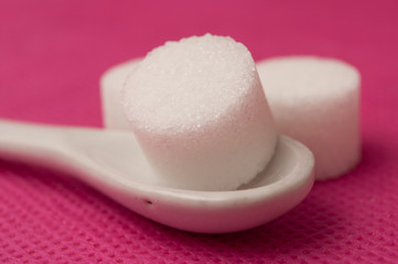  closeup of sugar in shaped circle in white spoon on pink background