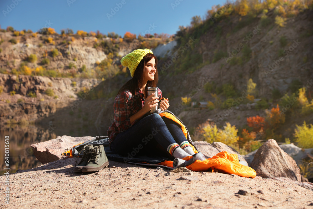 Sticker Female camper with thermos sitting on sleeping bag in wilderness