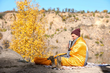 Male camper with thermos in sleeping bag outdoors. Space for text