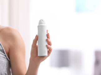 Beautiful young woman holding deodorant in room, closeup. Space for text