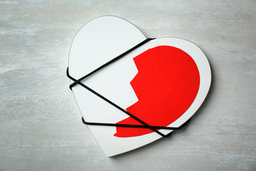 Half of cut paper heart tied with cord to detail on gray background, top view. Relationship problems