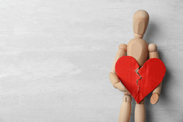 Wooden puppet holding torn cardboard heart on gray background, top view with space for text....