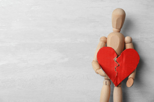 Wooden puppet holding torn cardboard heart on gray background, top view with space for text. Relationship problems