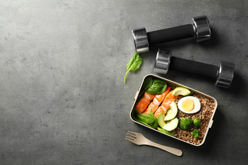 Container with natural healthy lunch, dumbbells and space for text on table, top view. High protein food