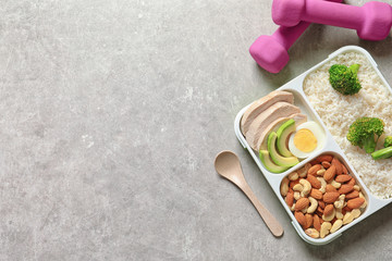 Container with natural healthy lunch, dumbbells and space for text on table, top view. High protein food