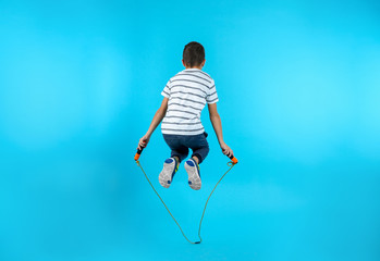 Active boy jumping rope on color background