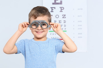 Little boy with trial frame near eye chart in hospital, space for text. Visiting children's doctor