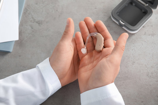 Doctor holding hearing aid at table, closeup. Medical device