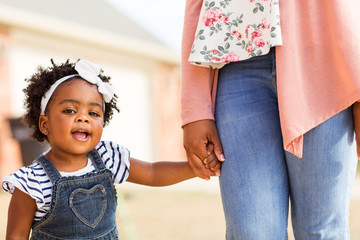 Little girl smiling and holding her mothers hand.