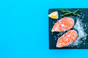 Fresh salmon steak with rosemary, lemon for cooking healthy food on blue background top view mock-up