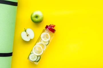 Healthy fruit water for sport, fitness. Bottle of water with lemon and cucumber near sport equipment on yellow background top view space for text