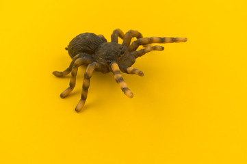 Toy spider from plastic on a yellow background.