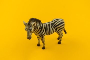 Toy zebra from plastic on a yellow background.
