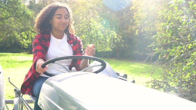 Beautiful African American mixed race teenage girl young woman driving a tractor through a sunny apple orchard eating an apple