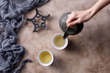 Still life with a traditional Asian herbal tea, which is poured from an old cast-iron kettle on a textured background.