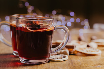 Mulled wine in mugs with scarf on wooden table.