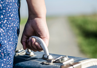 Refugee girl walking with her suitcase out of the road, closeup