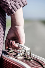 Refugee girl walking with her old suitcase out of the road