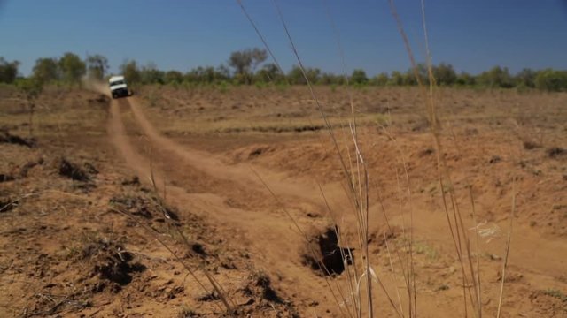 A wide shot of a truck convoy driving through the outback on a dry dusty arid road.