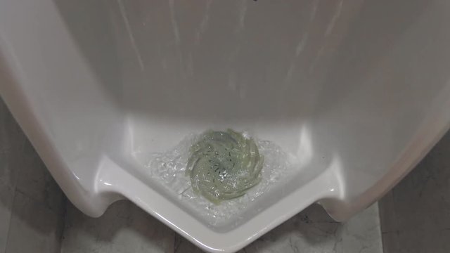Flushing water in white urinal for men in restroom, nobody
