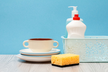 Bottles of dishwashing liquid in a basket and plates on blue background.