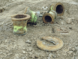 Old sewer manhole covered in soil on building side.