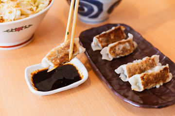 Gyoza (Japanese Pan-Fried Dumplings) held by chopsticks served with sauce and sesame oil.