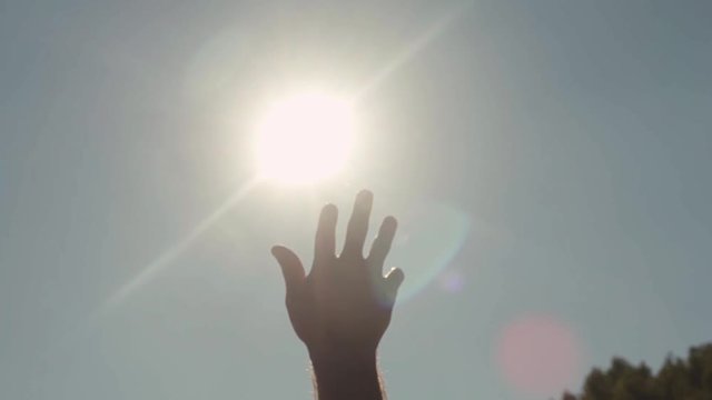 Close-up of hand reaching for sun. Stock. Bright sunlight breaks through fingers of outstretched hand to sky
