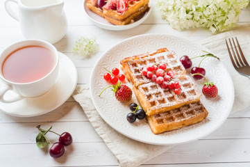Homemade waffles with summer berries on a plate. A Cup of tea on a light table. Selective focus