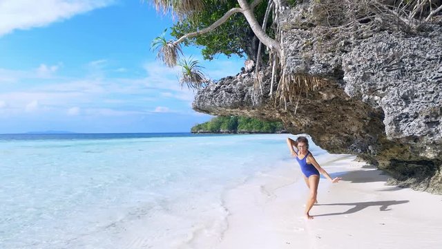 Slow motion: woman dancing on tropical beach, scenic turquoise water and white sand, Tomia Island, Wakatobi marine national park, Indonesia, paradise travel destination