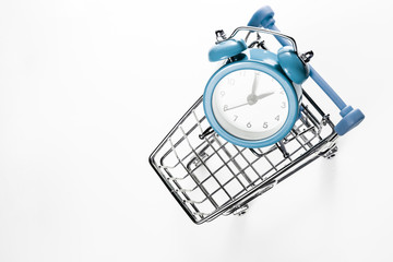 Blue alarm clock in the shopping trolley on a white background. Concept - time to buy. View from...