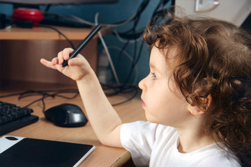Little 2 3 year old baby girl in white clothers draws at the home computer in graphics drawing...