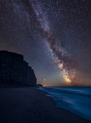 Vibrant Milky Way composite image over landscape of long exposure of West Bay in Dorset