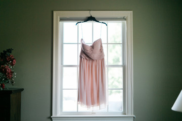 pink wedding dress hanging up near window