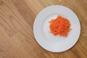A bit of ground carrot on white plate on wooden table