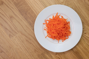 Ground carrot on white plate on wooden table