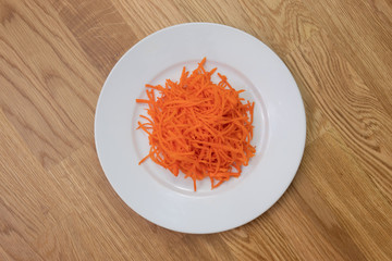 Ground carrot on white plate on wooden table centered