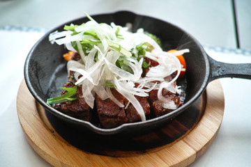 grilled beef steak served in an iron pan with sliced onion