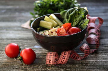 Bowl with porridge, fresh vegetables and measuring tape on wooden table. Diet food