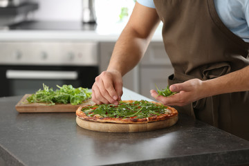 Young man decorating tasty pizza at table