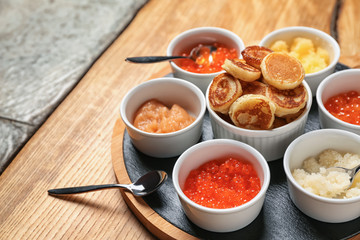 Set of tasty caviar with flapjacks on wooden table