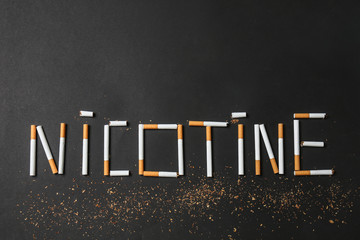 Word NICOTINE made with cigarettes on dark background. Concept of addiction