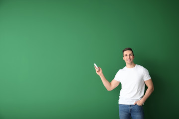 Young man with air conditioner remote control on color background